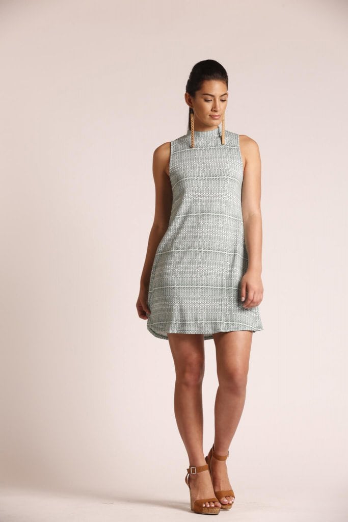 Female model wearing a turtleneck, sleeveless, short dress in sage green - Front View