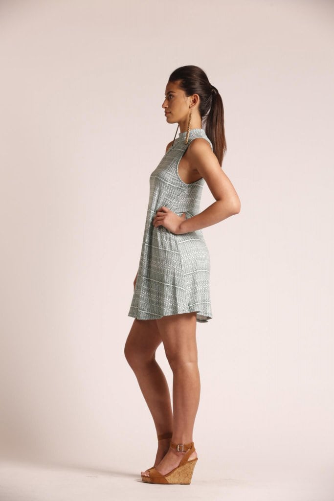 Female model wearing a turtleneck, sleeveless, short dress in sage green - Side View