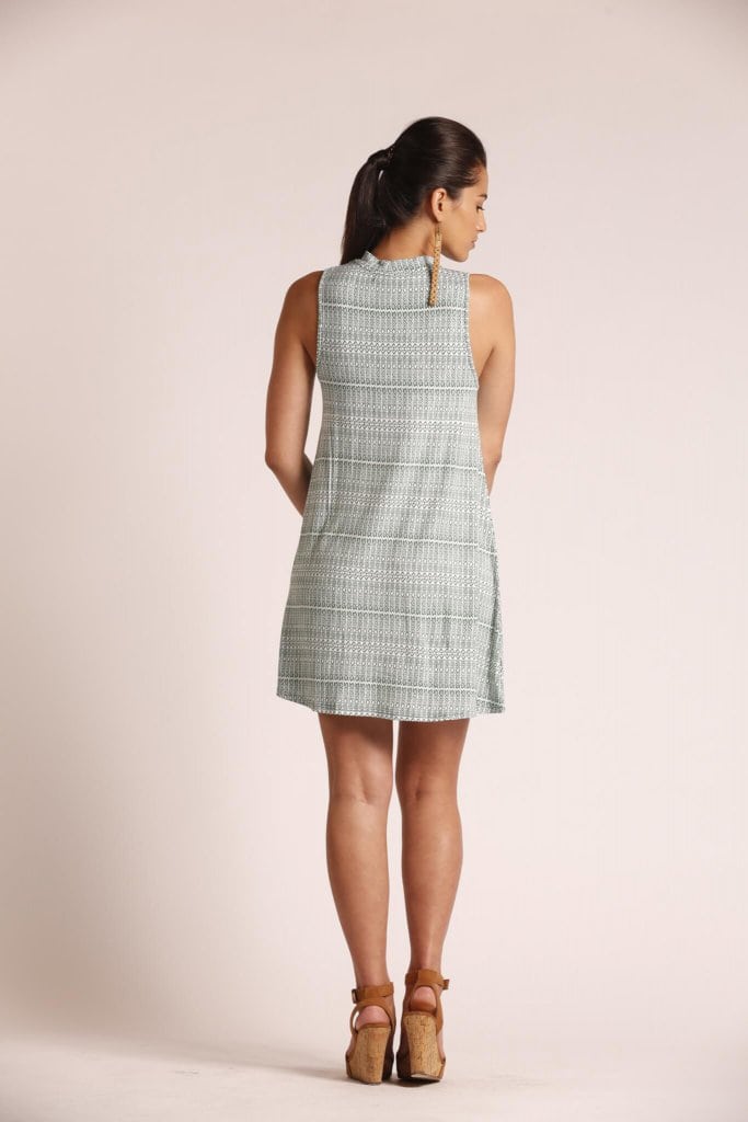 Female model wearing a turtleneck, sleeveless, short dress in sage green - Back View
