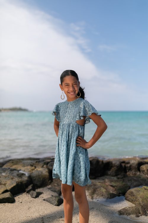 Girl model wearing a Keiki Kailani Dress in a Lei Kupee Print and Real Teal/Blue Tint Color - Front View