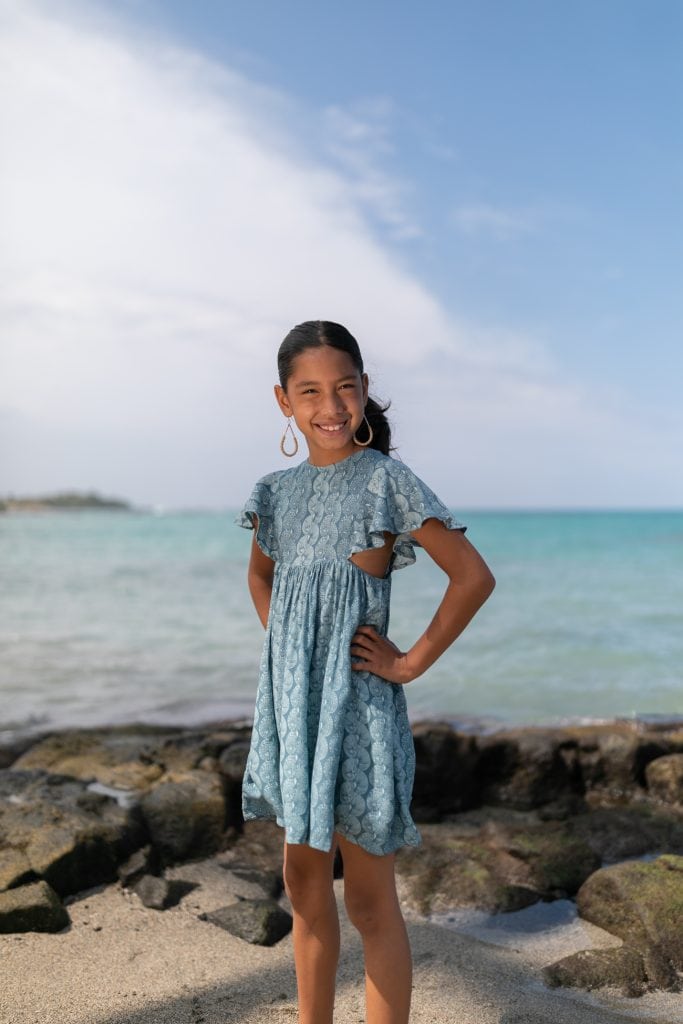 Girl model wearing a Keiki Kailani Dress in a Lei Kupee Print and Real Teal/Blue Tint Color - Front View