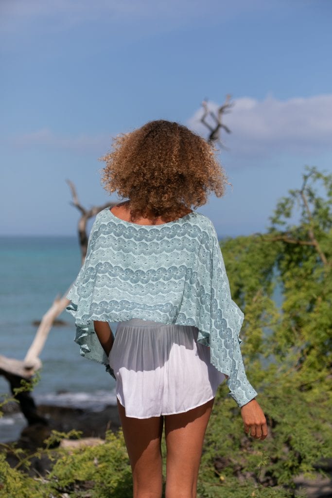 Female model wearing a Kikaha Top in Lei Kupee Print and Blue Tint/Real Teal - Back View