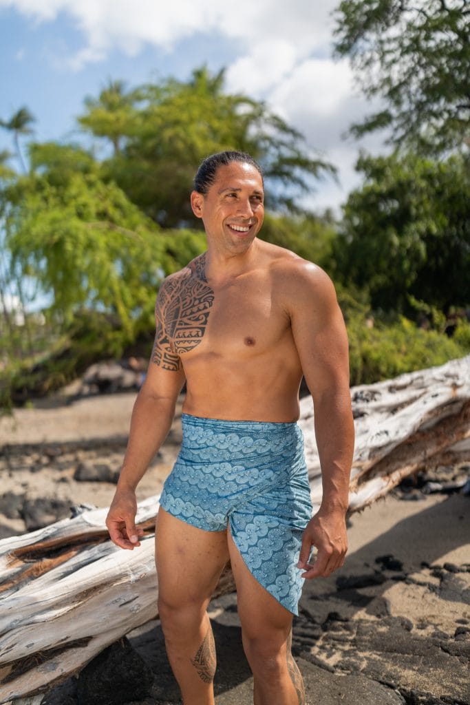 Male model wearing a pareo in Lei Kupee pattern and Real Teal and Blue Tint color - Front View